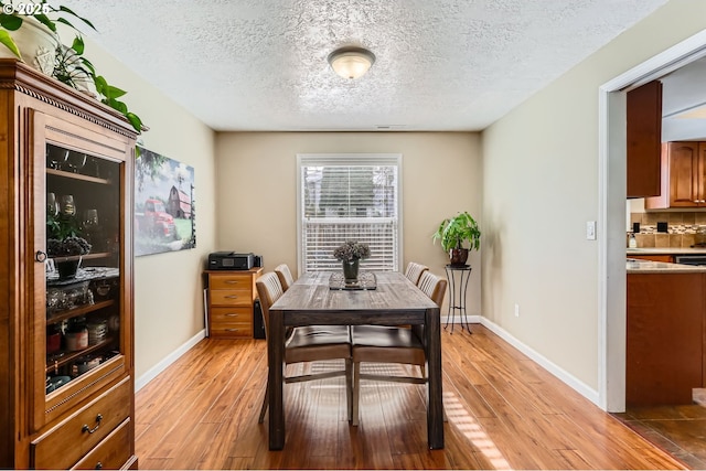 dining room with light wood-style flooring, baseboards, and a textured ceiling