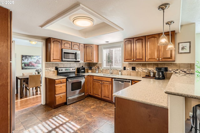 kitchen featuring stainless steel appliances, a peninsula, a sink, a tray ceiling, and tasteful backsplash