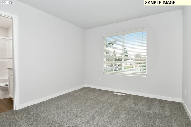 unfurnished bedroom with ensuite bath, baseboards, and dark carpet