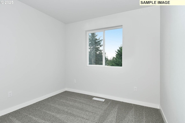 spare room with dark colored carpet, visible vents, and baseboards