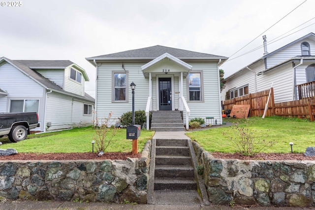 view of front of property with a front lawn, roof with shingles, and fence