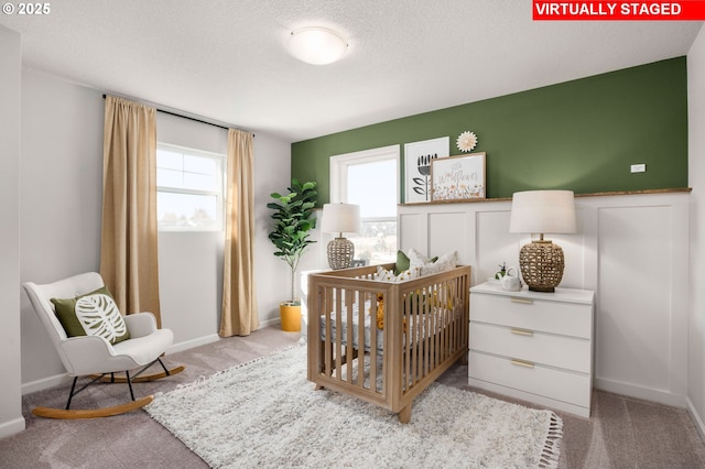 bedroom featuring a crib, light colored carpet, and a textured ceiling