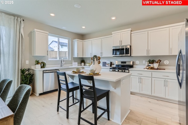 kitchen with stainless steel appliances, a breakfast bar, light countertops, and white cabinetry