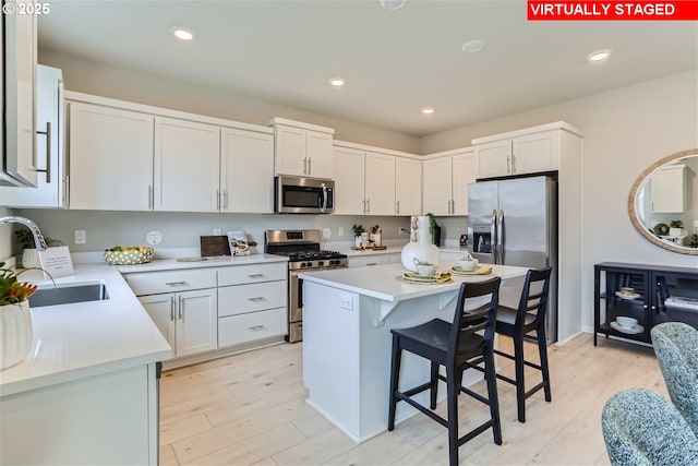 kitchen featuring stainless steel appliances, a breakfast bar, a sink, light countertops, and light wood finished floors