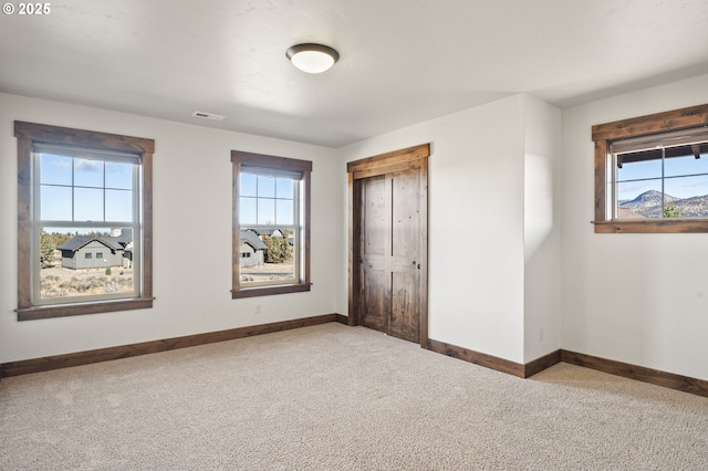 unfurnished bedroom featuring baseboards, visible vents, carpet flooring, and multiple windows