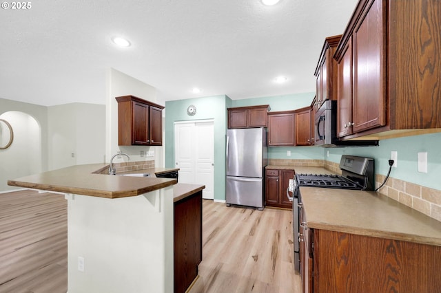 4908 Holly St, Springfield, OR 97478 - kitchen featuring appliances with stainless steel finishes, light wood-style flooring, a kitchen breakfast bar, a peninsula, and arched walkways