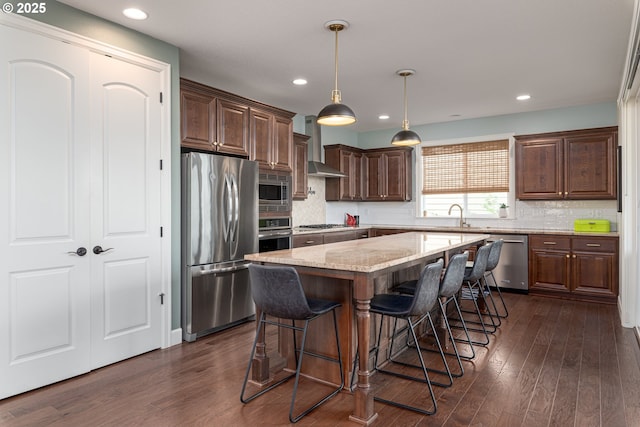 kitchen featuring appliances with stainless steel finishes, light stone counters, wall chimney exhaust hood, a center island, and dark wood-type flooring