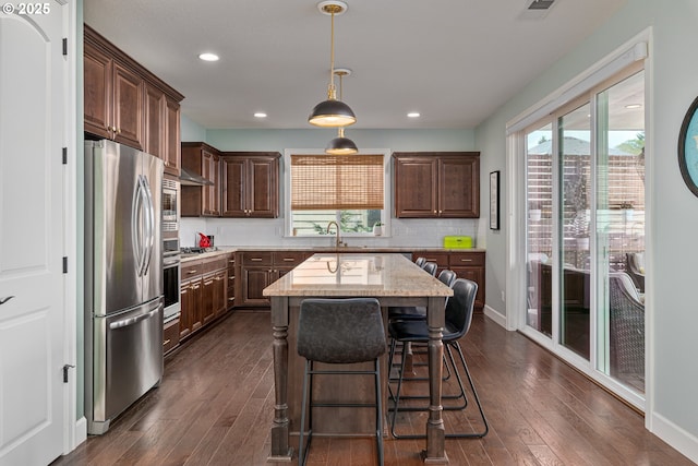 kitchen with dark brown cabinets, dark wood-style floors, tasteful backsplash, light stone counters, and appliances with stainless steel finishes