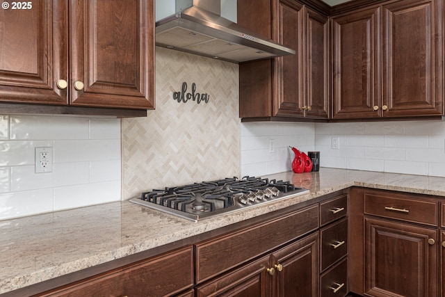 kitchen with wall chimney range hood, dark brown cabinetry, light stone countertops, stainless steel gas stovetop, and tasteful backsplash