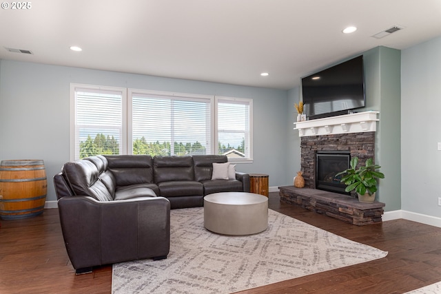 living area featuring visible vents, baseboards, wood finished floors, and a stone fireplace