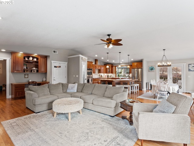 living room featuring ceiling fan with notable chandelier and light wood-type flooring