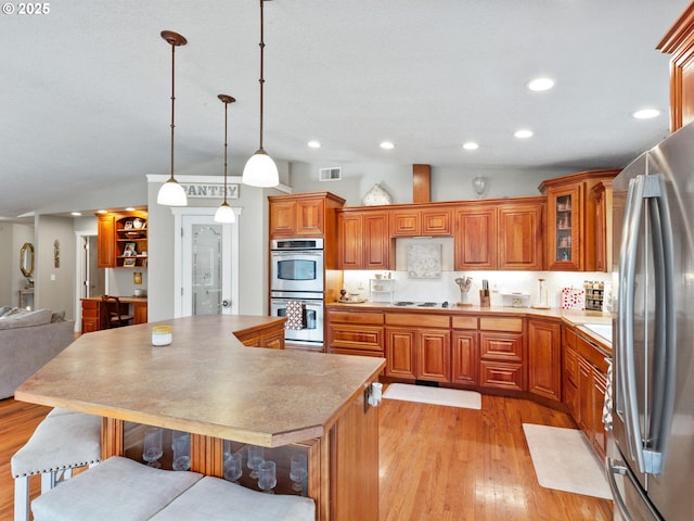 kitchen with pendant lighting, lofted ceiling, light hardwood / wood-style flooring, stainless steel appliances, and a kitchen island