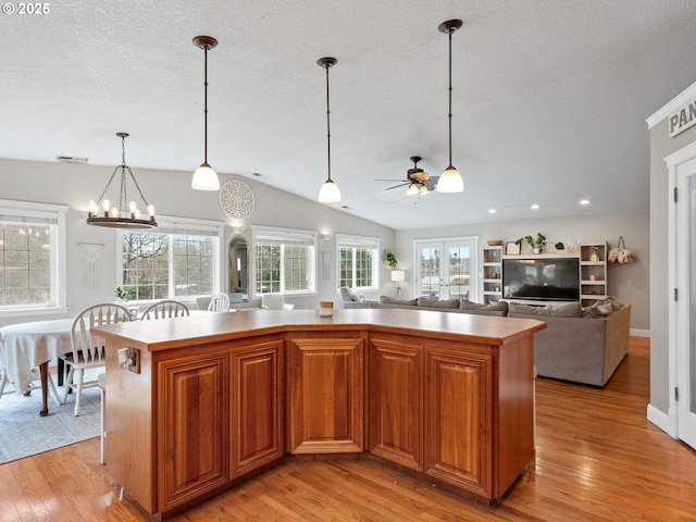 kitchen with vaulted ceiling, a kitchen island, decorative light fixtures, a textured ceiling, and light hardwood / wood-style flooring