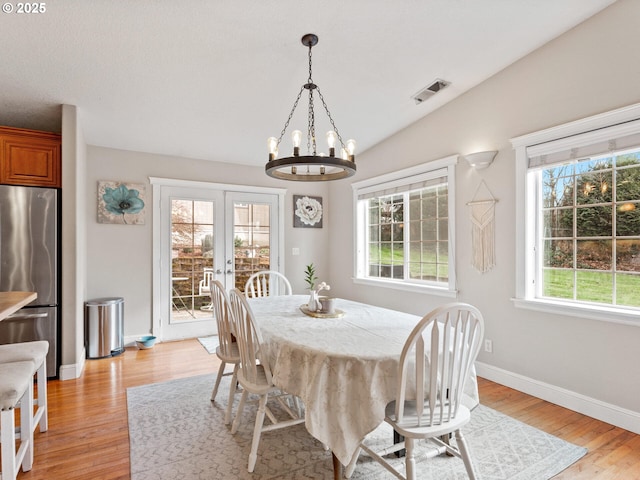 dining area featuring vaulted ceiling, an inviting chandelier, light wood-type flooring, and french doors