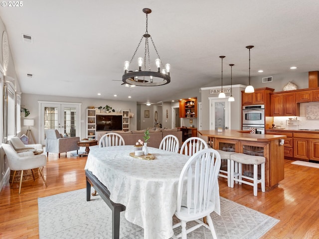 dining room featuring french doors, a chandelier, vaulted ceiling, and light hardwood / wood-style flooring