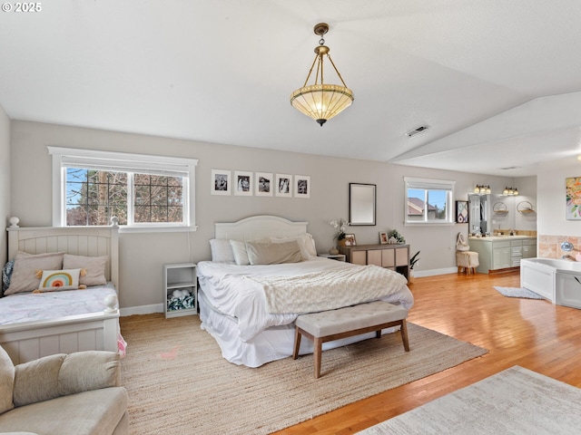 bedroom with vaulted ceiling, connected bathroom, and light wood-type flooring