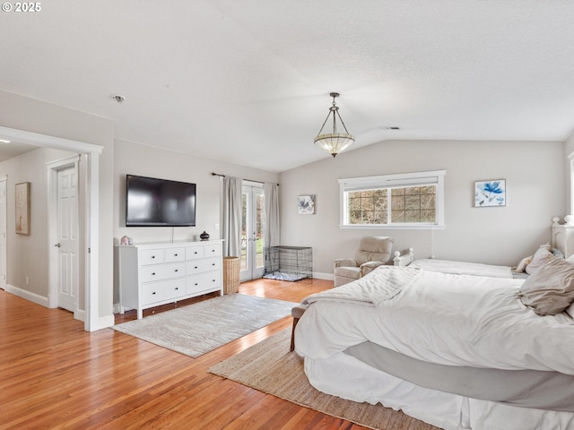 bedroom featuring lofted ceiling, light hardwood / wood-style floors, a textured ceiling, and access to outside