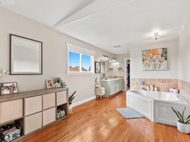 bathroom with a tub to relax in, hardwood / wood-style floors, vanity, and a textured ceiling