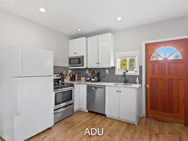 kitchen featuring sink, backsplash, stainless steel appliances, white cabinets, and light wood-type flooring