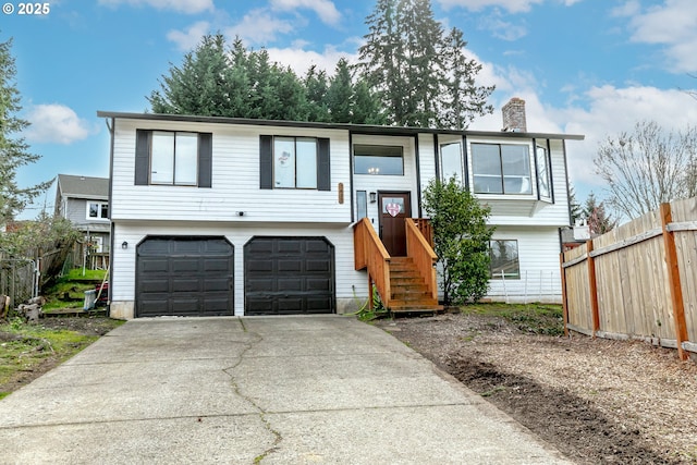 raised ranch with driveway, a chimney, an attached garage, and fence