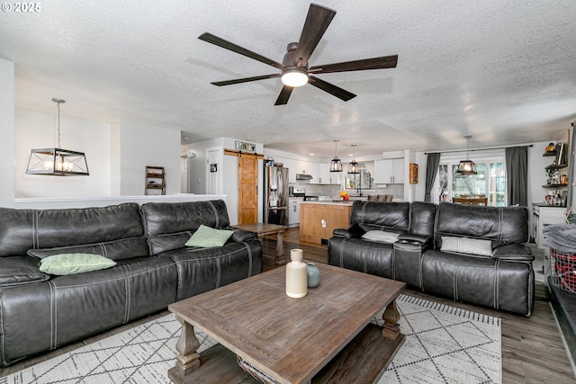 living area with a barn door, a textured ceiling, light wood-style flooring, and ceiling fan with notable chandelier