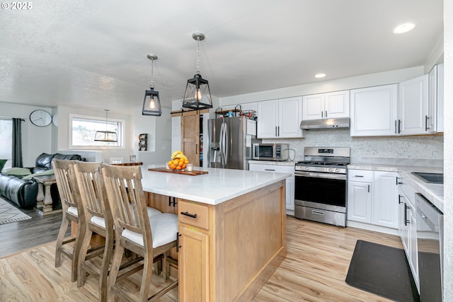 kitchen featuring light wood finished floors, a kitchen island, under cabinet range hood, and stainless steel appliances