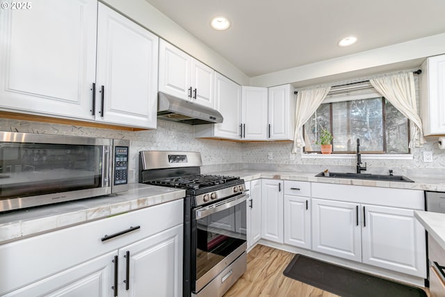 kitchen with under cabinet range hood, a sink, white cabinetry, stainless steel appliances, and light countertops