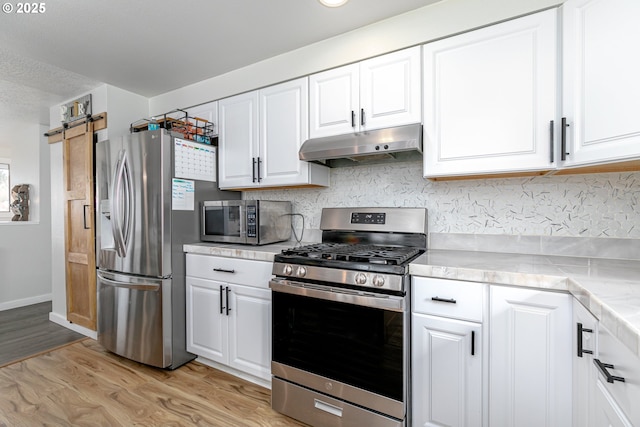 kitchen featuring under cabinet range hood, a barn door, light wood-style flooring, white cabinets, and stainless steel appliances