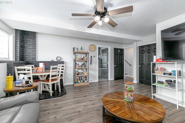 living room with a ceiling fan, wood finished floors, baseboards, and a textured ceiling