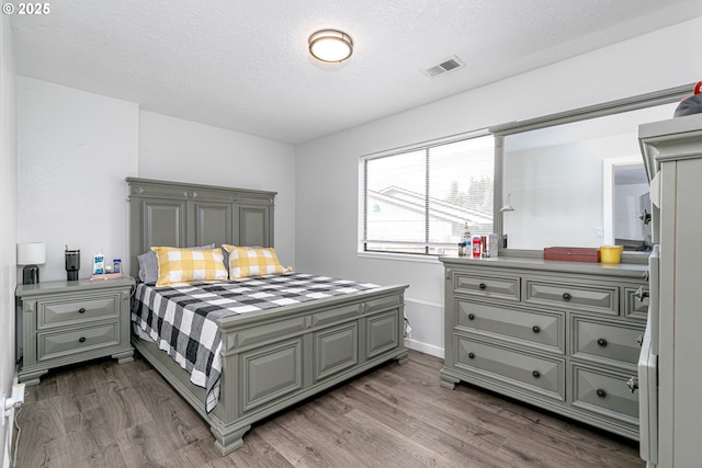 bedroom featuring wood finished floors, visible vents, and a textured ceiling