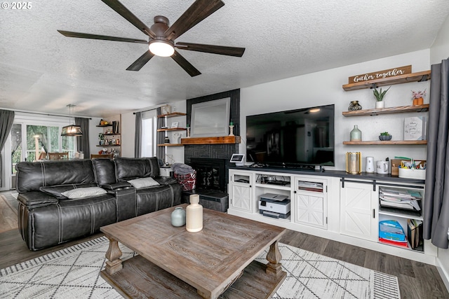 living area with a ceiling fan, a brick fireplace, wood finished floors, and a textured ceiling