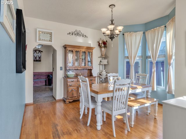 dining area with a chandelier, light wood-type flooring, arched walkways, and baseboards