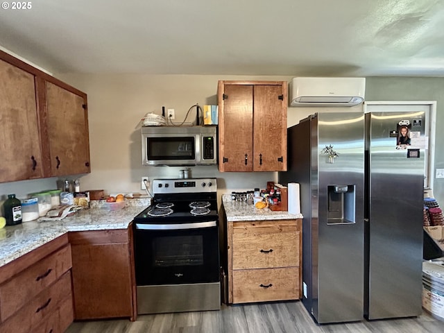 516 W Railroad Ave, Goldendale, WA 98620 - kitchen with wood finished floors, brown cabinets, stainless steel appliances, light stone counters, and a wall mounted AC