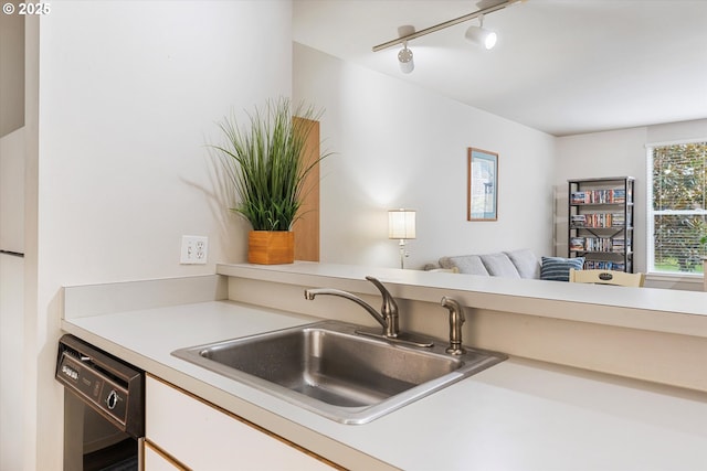 kitchen featuring black dishwasher, a sink, rail lighting, light countertops, and open floor plan