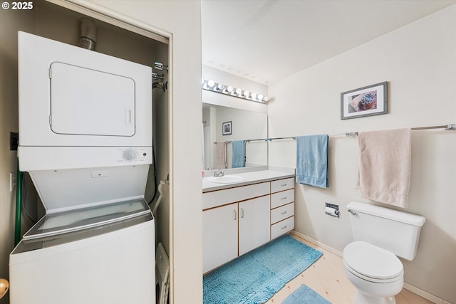 bathroom featuring stacked washing machine and dryer, baseboards, toilet, and vanity