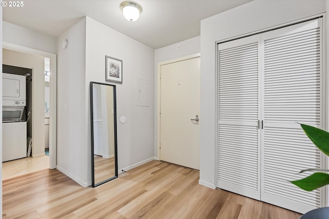 entryway with stacked washer / dryer, light wood-style floors, and baseboards