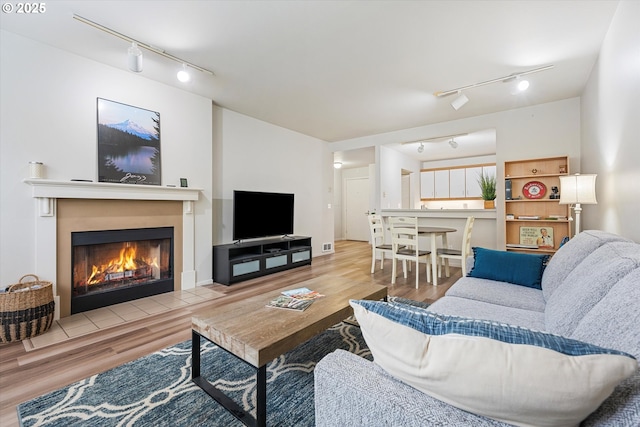 living room featuring rail lighting, wood finished floors, and a glass covered fireplace