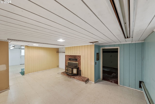 finished below grade area featuring tile patterned floors, wooden walls, and a wood stove