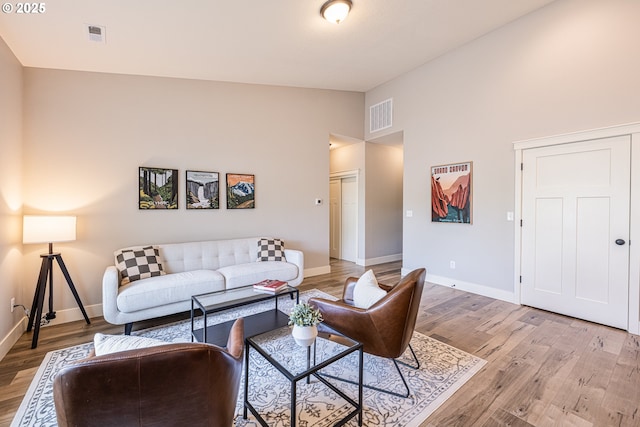 living area with baseboards, visible vents, vaulted ceiling, and light wood-type flooring