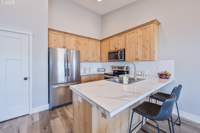 kitchen featuring light brown cabinetry, stainless steel appliances, a sink, and a peninsula
