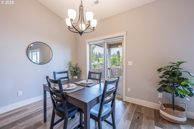 dining room featuring a notable chandelier, baseboards, wood finished floors, vaulted ceiling, and visible vents