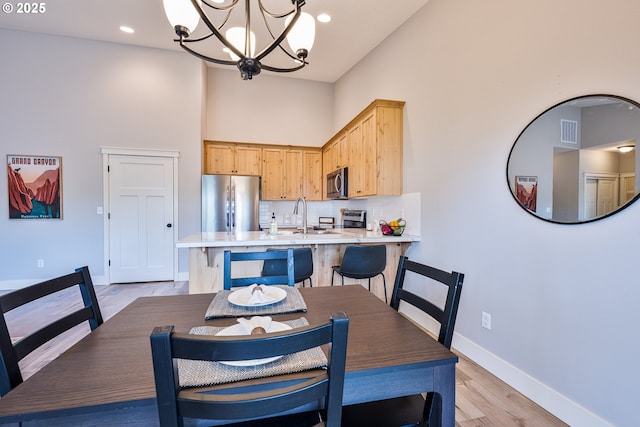 dining space featuring a towering ceiling, visible vents, baseboards, a notable chandelier, and light wood-style flooring