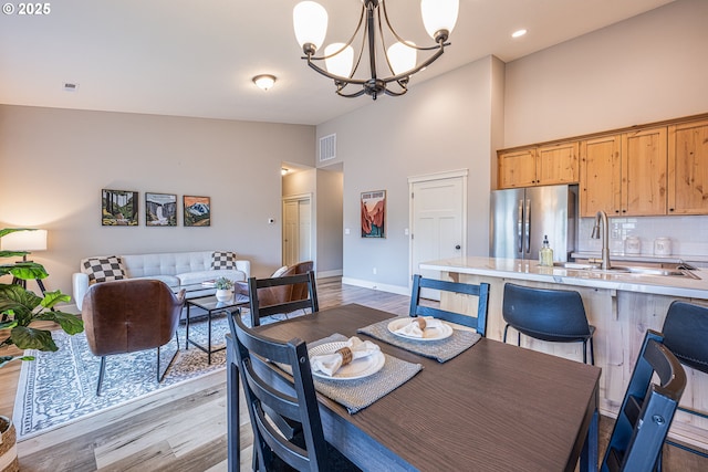 dining space featuring a towering ceiling, visible vents, light wood-type flooring, baseboards, and a notable chandelier