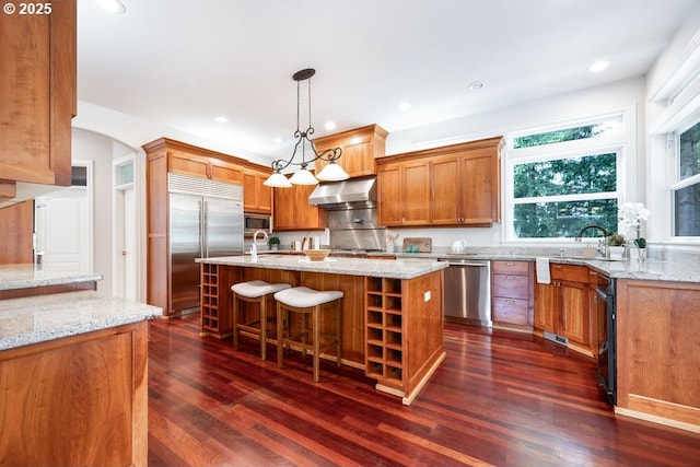 3830 NW 142nd Ter, Portland, OR 97229 - kitchen featuring stainless steel appliances, ventilation hood, an island with sink, dark wood-style floors, and light stone countertops