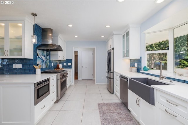 kitchen featuring light tile patterned floors, appliances with stainless steel finishes, white cabinets, a sink, and wall chimney range hood