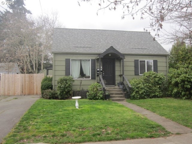 bungalow-style house with a shingled roof, fence, and a front lawn