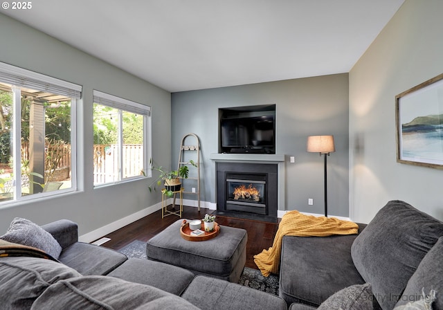 living room with dark wood-type flooring, visible vents, baseboards, and a glass covered fireplace