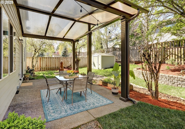 view of patio with a storage shed, outdoor dining space, a fenced backyard, and an outdoor structure
