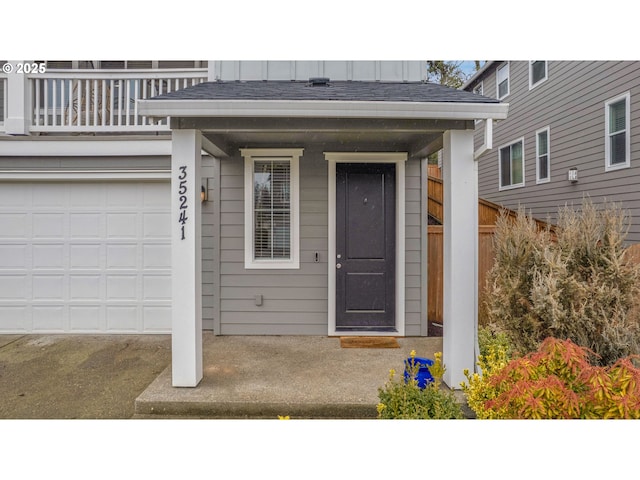 entrance to property with roof with shingles, board and batten siding, fence, and a balcony