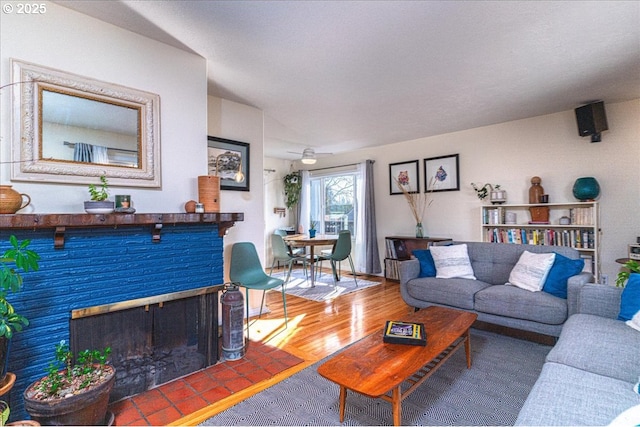 living room featuring hardwood / wood-style flooring, ceiling fan, and a brick fireplace